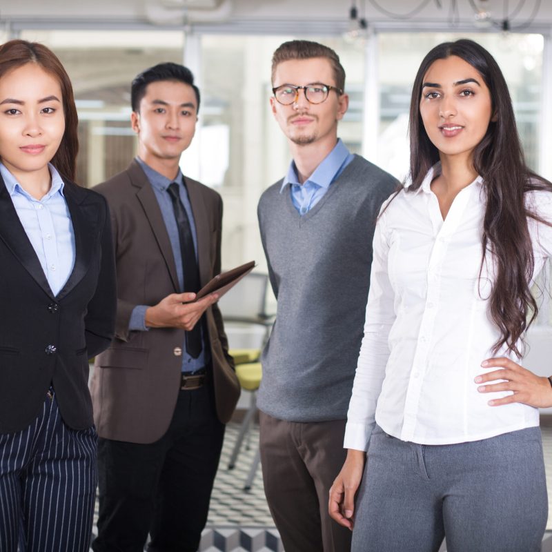 Closeup portrait of four confident young business people looking at camera and standing with cafe interior in background